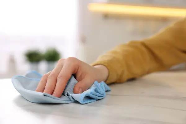 Woman with microfiber cloth cleaning white marble table in kitchen, closeup