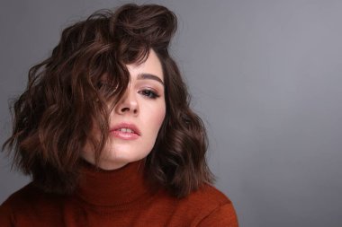 Gri arka planda dalgalı saç stili olan güzel bir genç kadın. Metin için boşluk