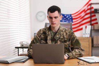 Askerlik. Ofisteki ahşap masada dizüstü bilgisayarla çalışan genç asker.