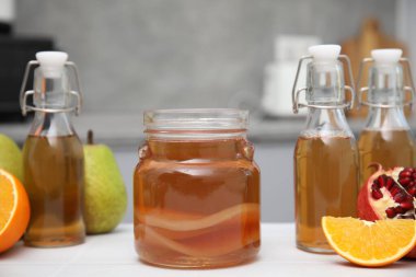 Ev yapımı mayalanmış kombu çayı ve mutfaktaki beyaz masada taze meyveler.