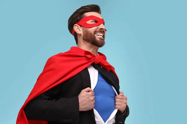 Happy businessman wearing superhero costume under suit on light blue background. Space for text