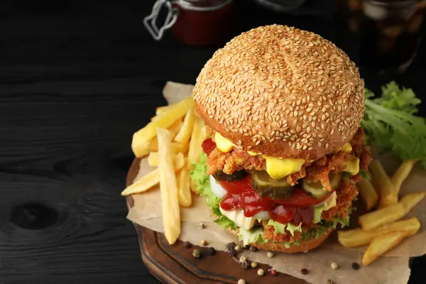 Delicious burger with crispy chicken patty and french fries on black wooden table, closeup. Space for text