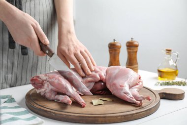 Beyaz ahşap masada bütün tavşanı kesen kadın, yakın plan.