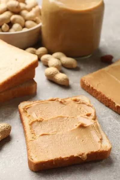 Tasty peanut butter sandwiches and peanuts on gray table, closeup