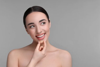 Gri arka planda vitamin hapı olan güzel bir genç kadın. Metin için boşluk