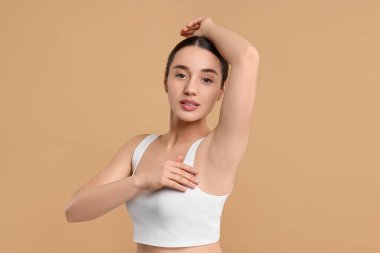 Güzel bir kadın bej arka planda pürüzsüz, temiz bir ciltle koltukaltı gösteriyor.