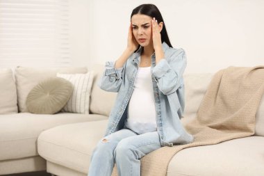 Evdeki kanepede baş ağrısı çeken hamile bir kadın.