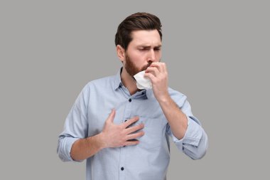 Açık gri arka planda öksüren hasta bir adam.