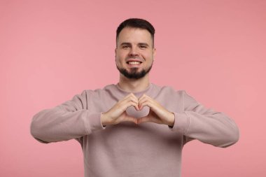 Pembe arka planda elleri olan bir adam kalp hareketi gösteriyor.