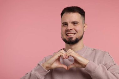 Pembe arka planda elleri olan bir adam kalp hareketi gösteriyor.