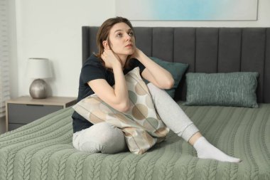 Evdeki yatakta oturan üzgün genç kadın.