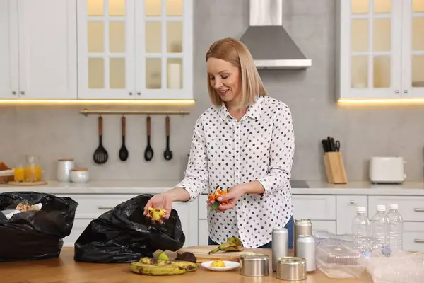 Smiling woman separating garbage at table in kitchen