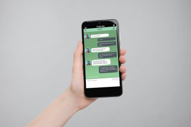 Akıllı telefondaki mesajlaşma uygulamasını gri arka planda kullanan bir kadın, yakın plan