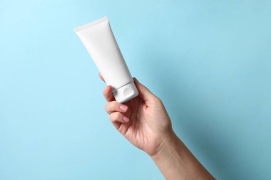 Açık mavi arka planda el kremi tüpü olan kadın, yakın plan.