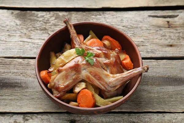 Tasty cooked rabbit with vegetables in bowl on wooden table