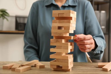 Jenga oynuyorum. Kapalı alandaki ahşap masada, kuleden bloğu kaldıran kadın.