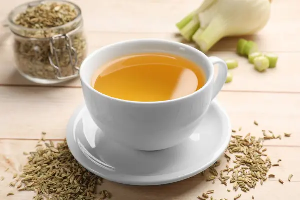 Fennel tea in cup, seeds and fresh vegetable on light wooden table, closeup