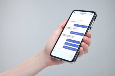 Akıllı telefondaki mesajlaşma uygulamasını gri arka planda kullanan bir kadın, yakın plan