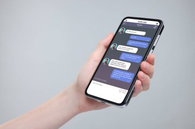 Akıllı telefondaki mesajlaşma uygulamasını gri arka planda kullanan bir kadın, yakın plan