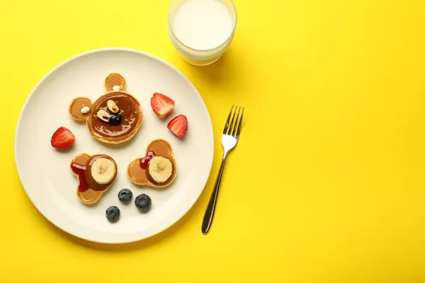 Creative serving for kids. Plate with cute bears made of pancakes, berries, banana and chocolate paste on yellow background, flat lay. Space for text