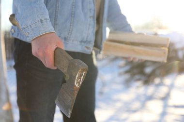 Güneşli kış gününde baltalı ve odunlu bir adam, yakın plan.
