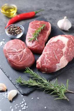 Gri arka planda çiğ biftek, yağ ve baharatlar, yakın plan.