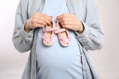 Beyaz arka planda bebek ayakkabıları olan hamile kadın, yakın plan.