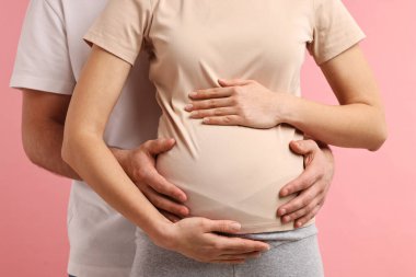 Adam hamile eşinin karnına dokunuyor pembe arka planda, yakın plan.