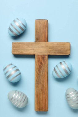 Ahşap haç ve açık mavi arka planda Paskalya yumurtaları, düz yatıyordu.