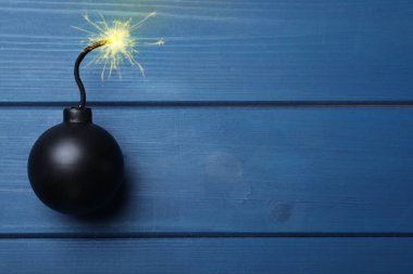 Old fashioned black bomb with lit fuse on blue wooden table, top view. Space for text clipart
