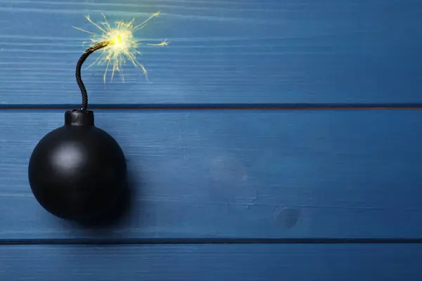 stock image Old fashioned black bomb with lit fuse on blue wooden table, top view. Space for text