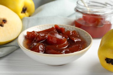 Lezzetli ev yapımı ayva reçeli kasede ve beyaz ahşap masada meyveler, yakın plan.