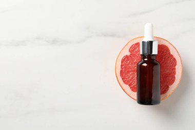 Şişede greyfurt yağı ve beyaz mermer masa üzerinde yarım meyve. Metin için boşluk