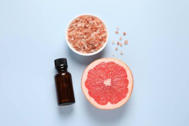 Şişede greyfurt yağı, deniz tuzu ve açık mavi masada meyve kesimi.