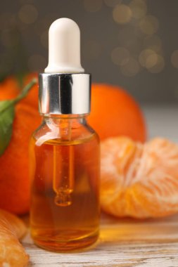 Bir şişe mandalina yağı ve beyaz ahşap masada taze meyveler, yakın plan.