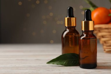 Mandalina yağı şişeleri ve beyaz ahşap masa üzerinde yeşil yaprak, yakın plan. Metin için boşluk