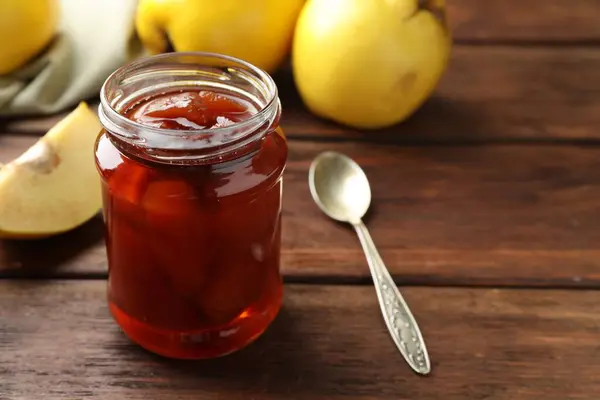 Tasty homemade quince jam in jar on wooden table, closeup. Space for text