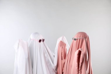 Büyüleyici hayaletler. Açık gri arka planda güneş gözlüklü, renkli çarşaflı kadınlar