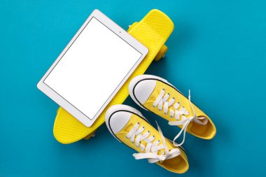 Modern tablet, kaykay ve açık mavi arka planda ayakkabılar. Metin için boşluk