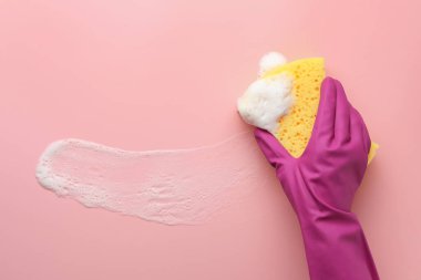 Lastik eldivenli temizleyici süngeri pembe arka planda tutuyor..