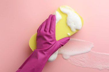 Lastik eldivenli temizleyici süngeri pembe arka planda tutuyor..