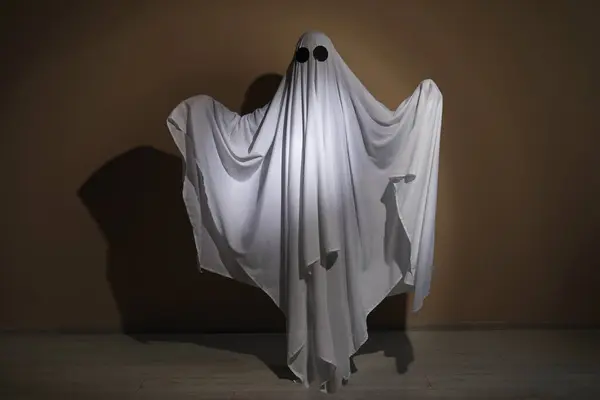 Creepy ghost. Woman covered with sheet near brown wall