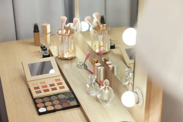 Different beauty products and perfumes on wooden dressing table in room