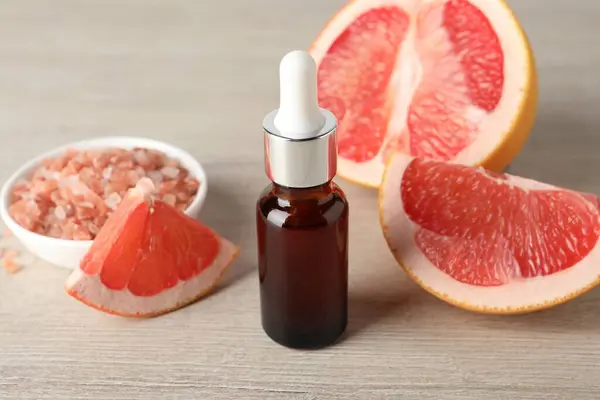 Grapefruit essential oil in bottle, sea salt and fruit on light wooden table, closeup