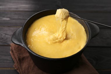 Jambonu fondü kabına daldırmak, erimiş peyniri siyah ahşap masaya koymak, yakın plan.