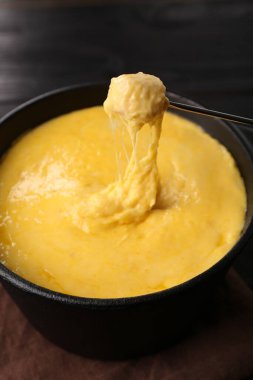 Jambonu fondü kabına daldırmak, erimiş peyniri siyah ahşap masaya koymak, yakın plan.