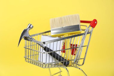 Sarı arka planda boya ve yenileme ekipmanları olan küçük bir alışveriş arabası.