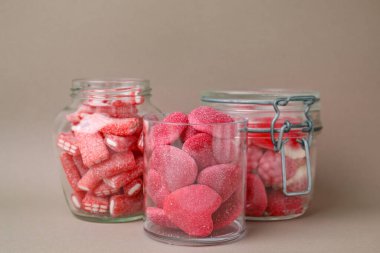 Cam kavanozlarda açık kahverengi arka planda lezzetli pembe şekerler.