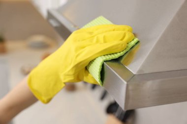 İçinde sprey şişesi ve mikrofiber bez olan bir kadın mutfak kaputunu temizliyor.