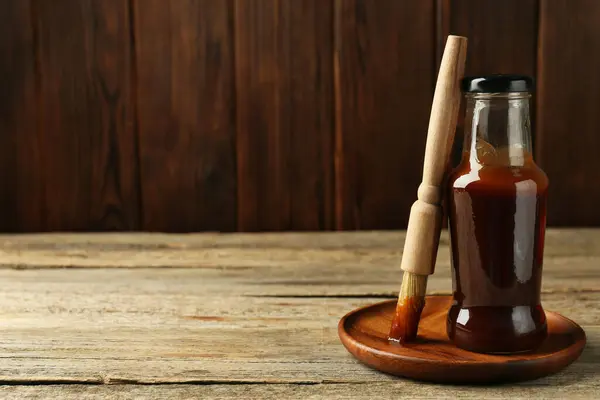 Tasty barbeque sauce in bottle and brush on wooden table. Space for text